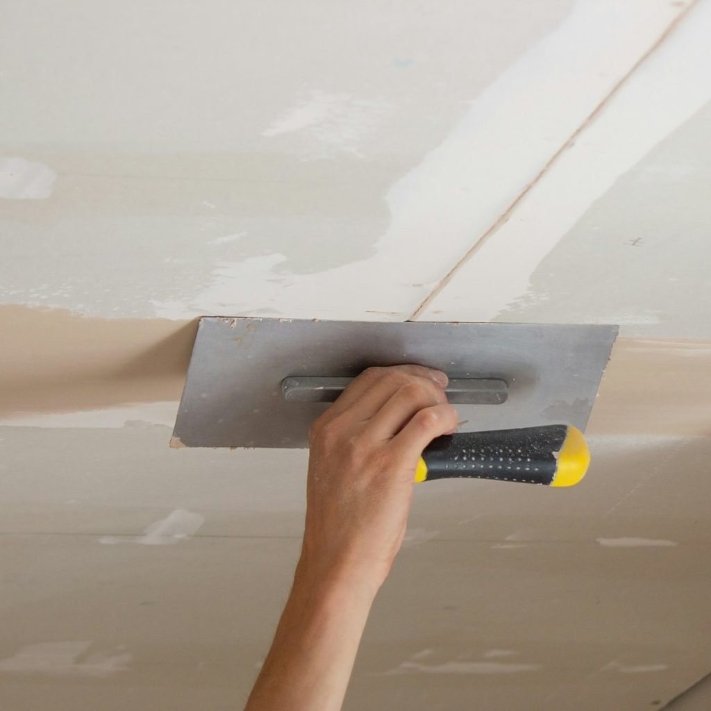 A man puts putty on a plasterboard ceiling. Putty for the joints of plasterboard sheets