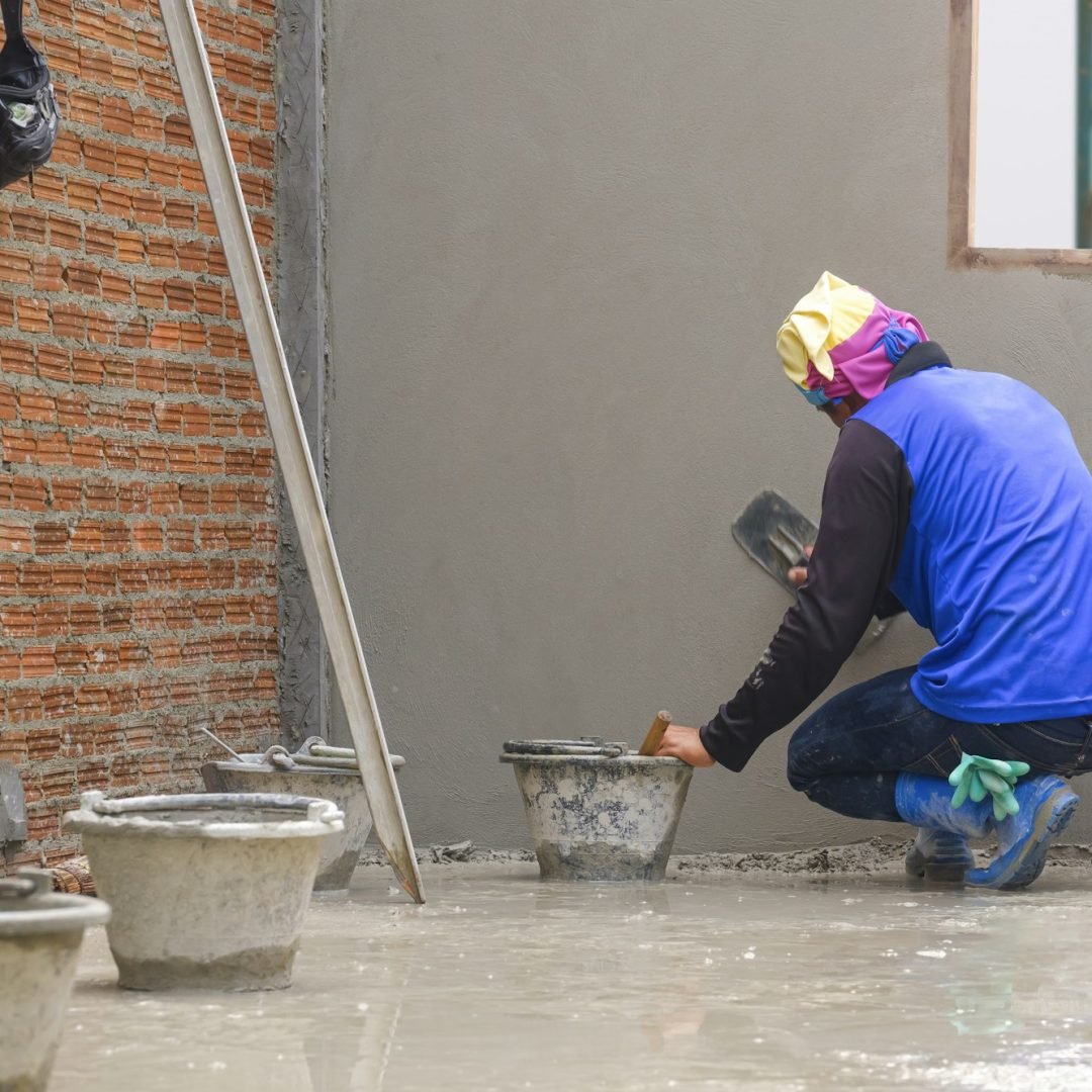 Rear side view of Asian builder using trowel to polishing concrete wall in house construction site